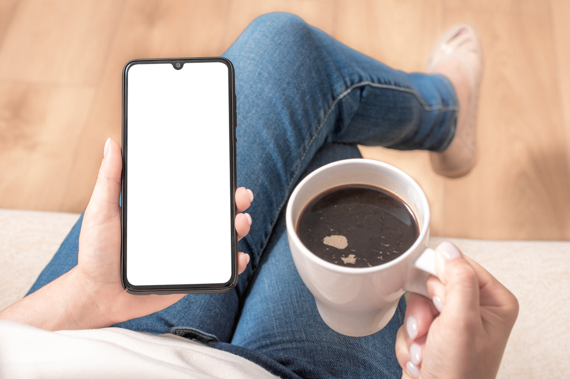Mockup cellphone. Mockup image of woman's hands holding mobile phone with blank screen on thigh and coffee cup.
